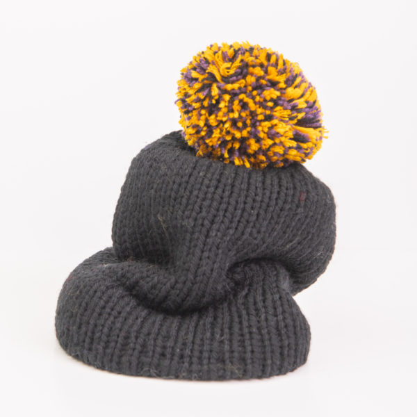 Bonnet avec pompon noir, jaune et violet tricoté avec un mélange de laines. Réalisé par Charlotte Tricote.